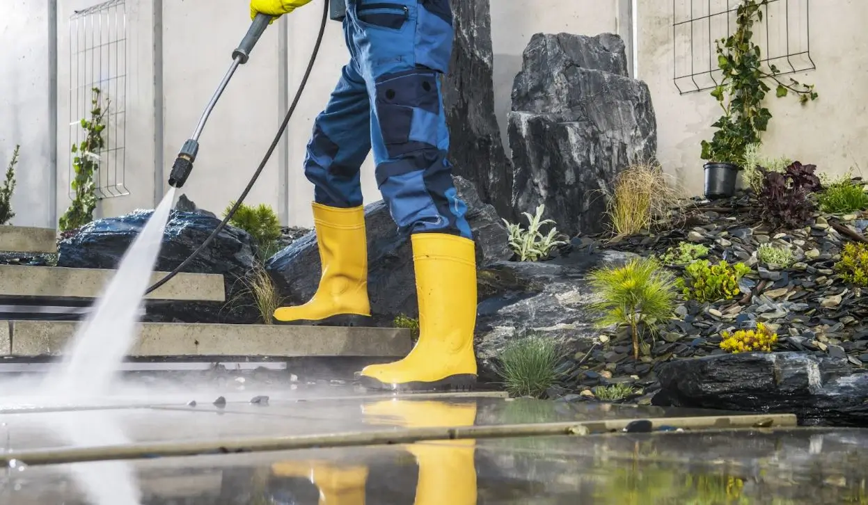 A cropped shot of a man in yellow rubber boots using a pressure wash on architectural concrete elements in his garden.