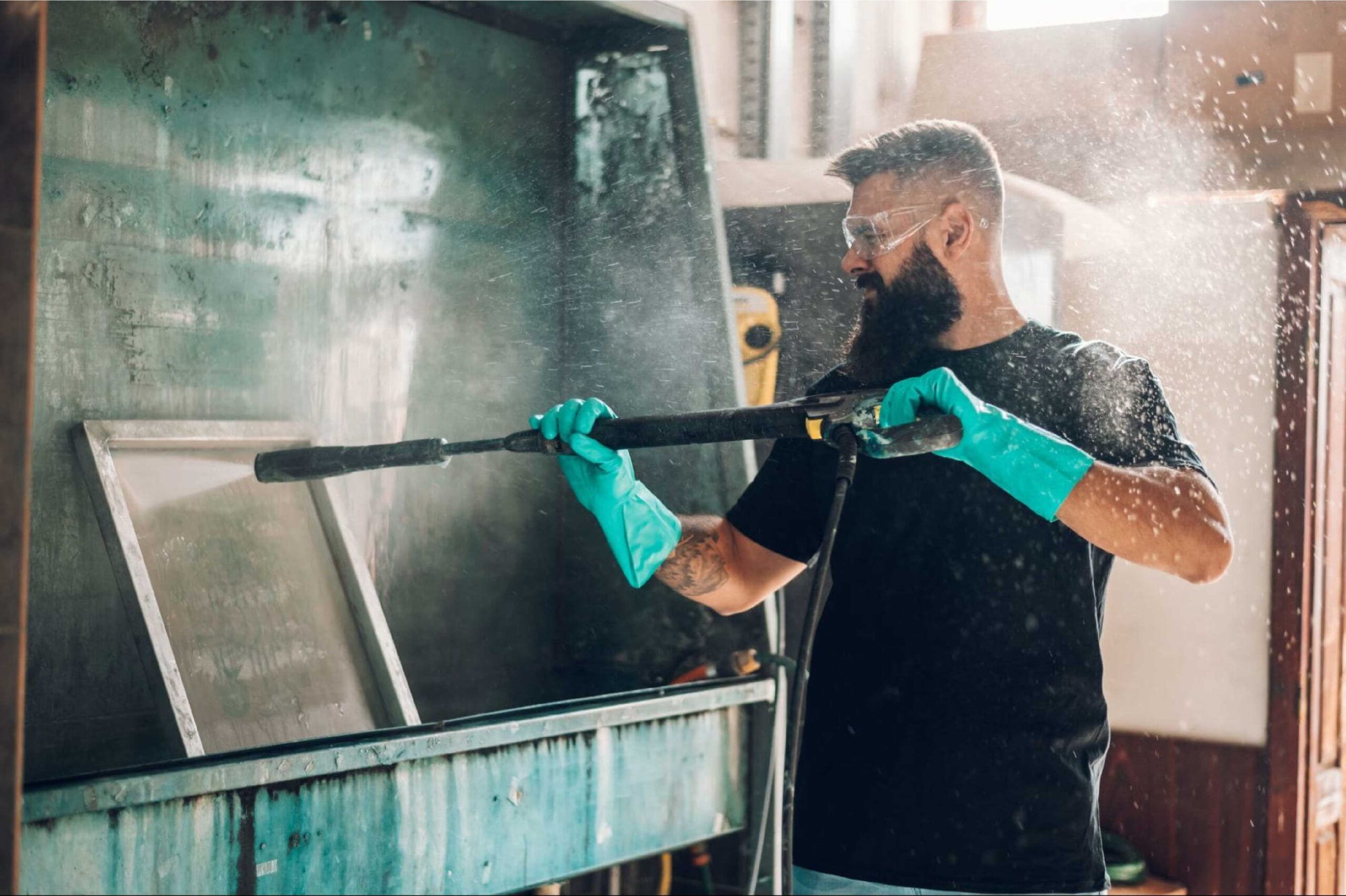 A man sprays a screen frame with a pressure washer in a print shop.