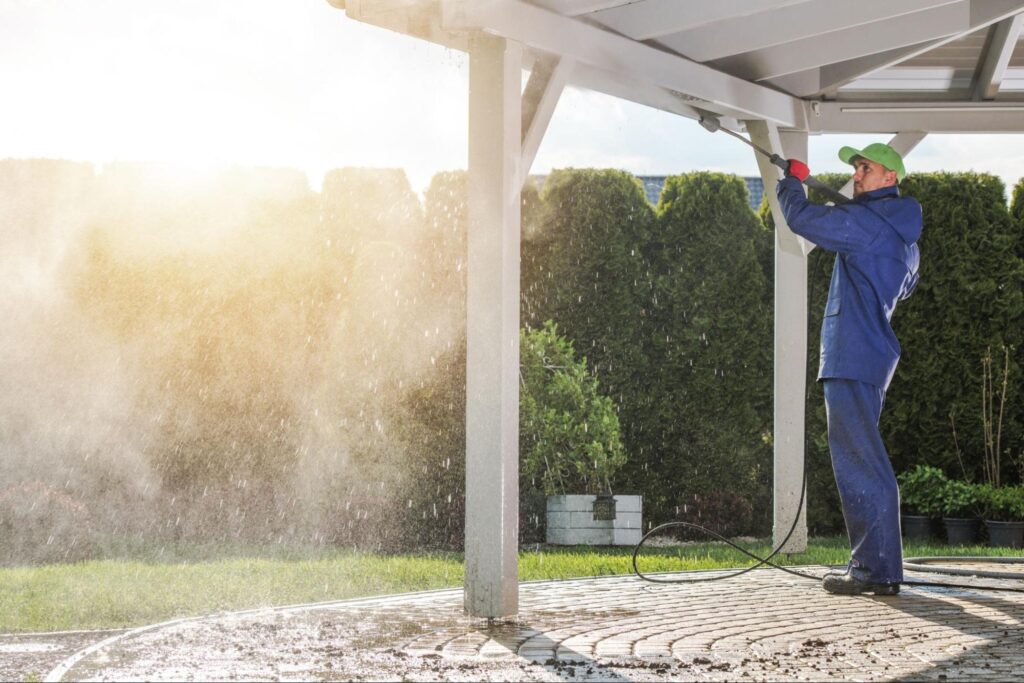 A man cleans an outdoor pergola with a pressure washer.