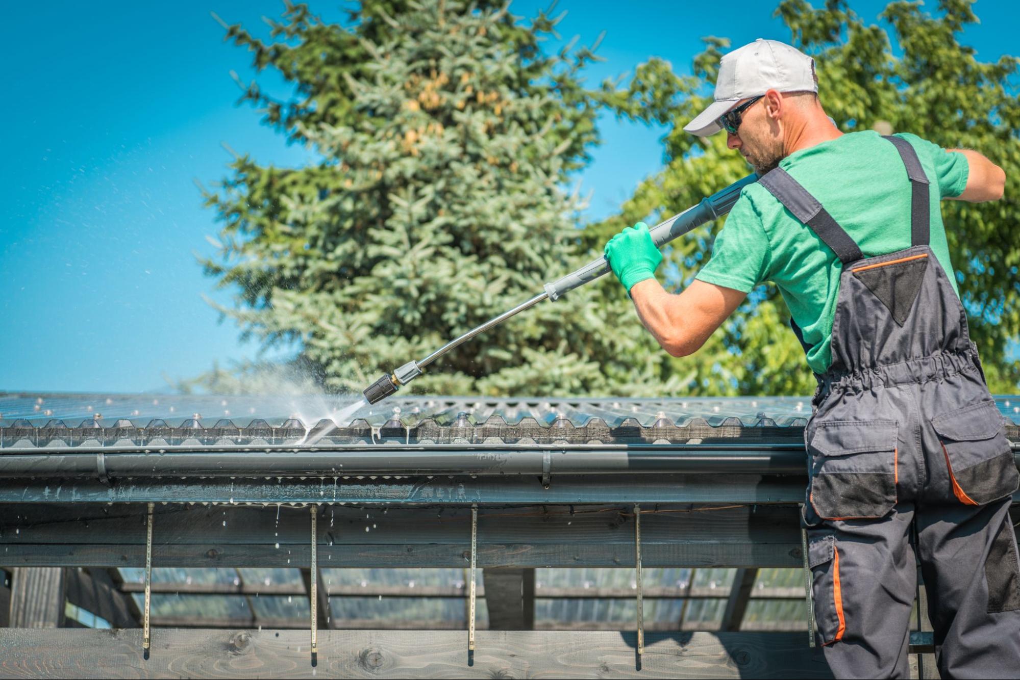 A man is using a power washer to clean roof gutters.