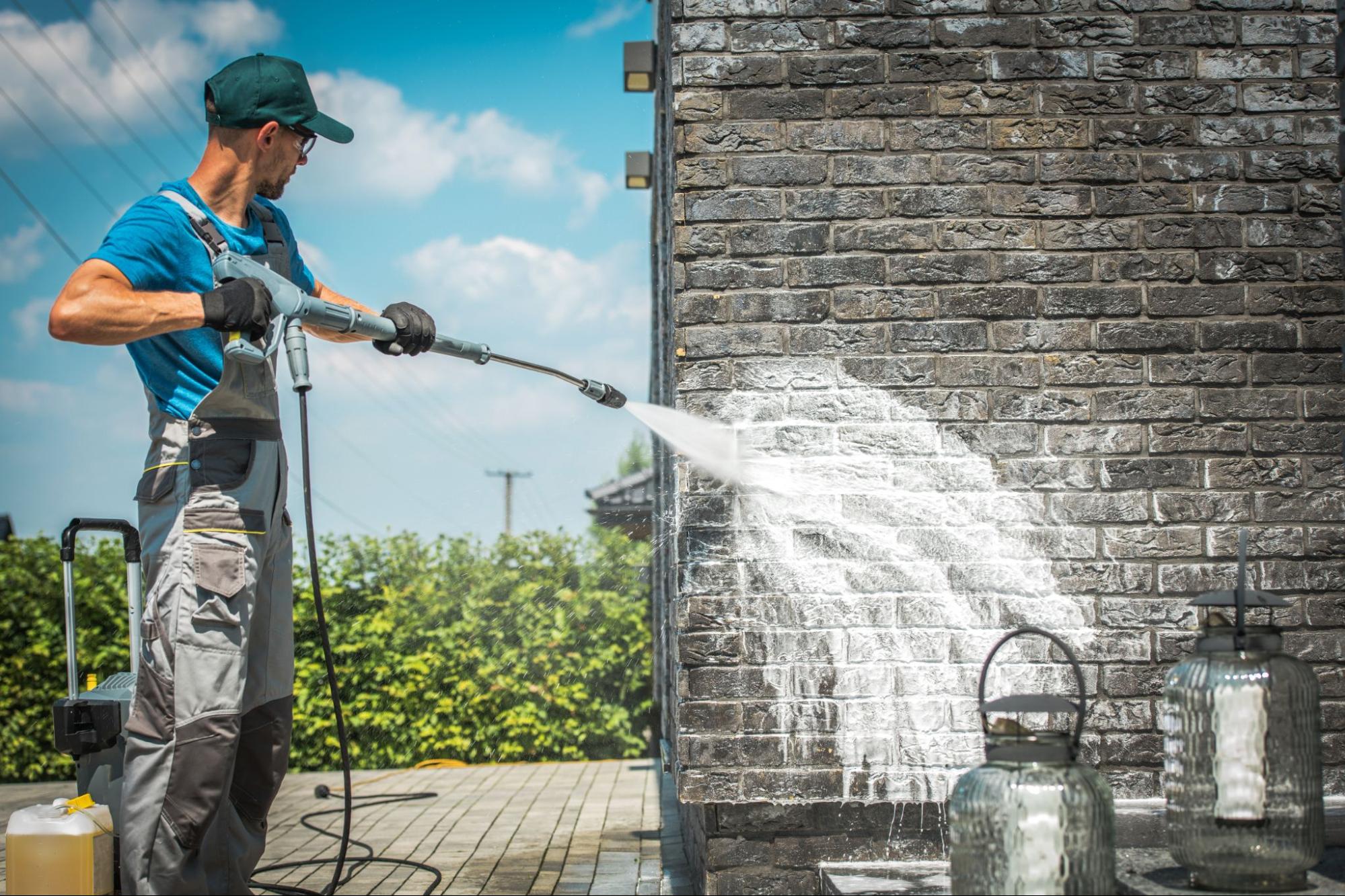 A worker cleaning a brick wall using a high-pressure washer