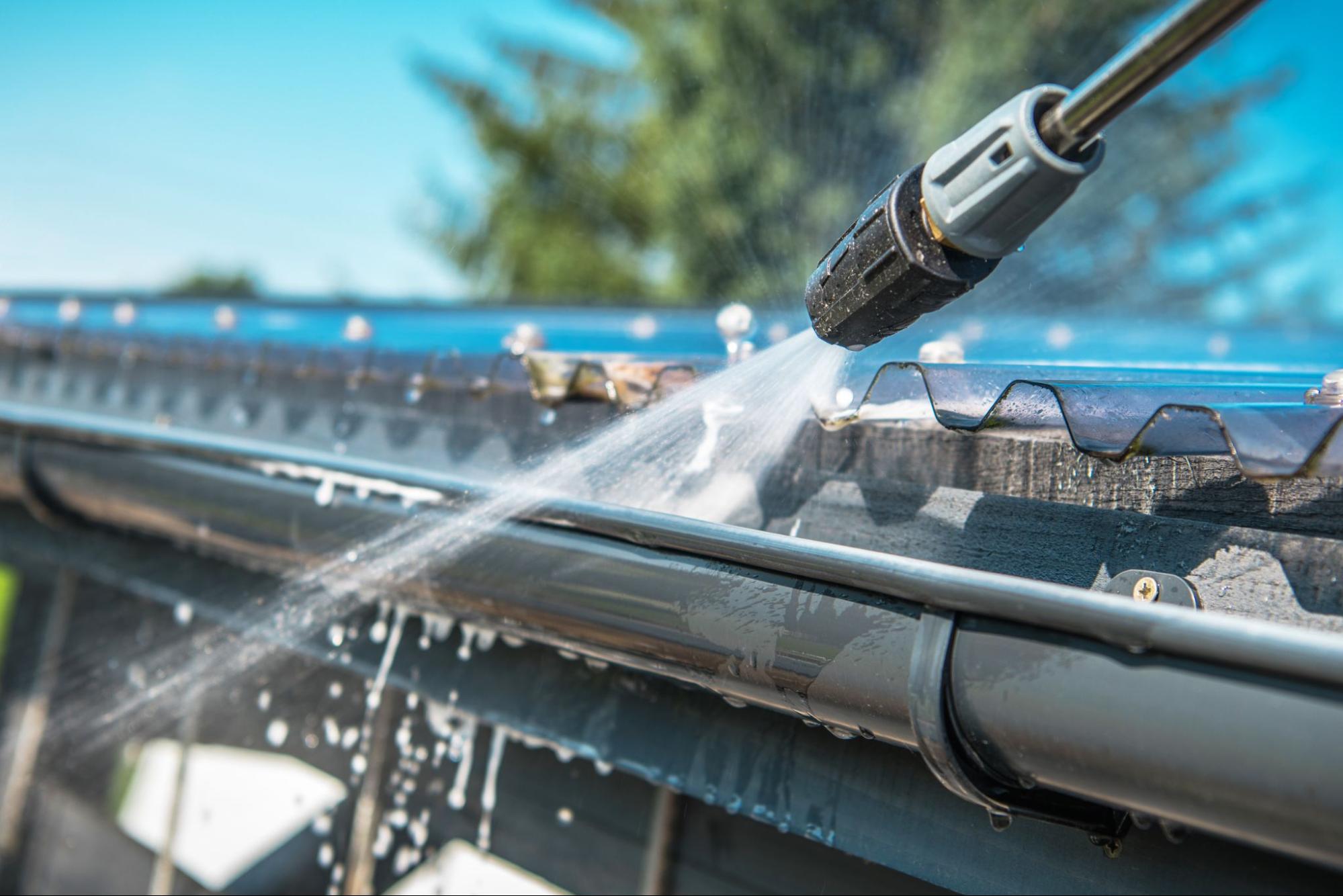 Closeup on a pressure washer spraying into a house gutter.