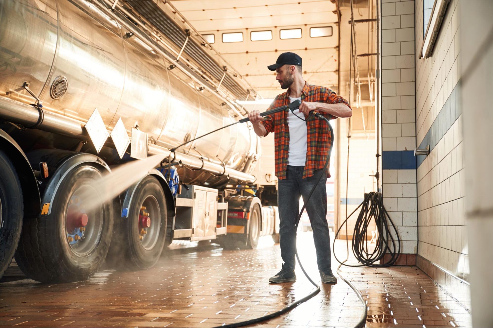 A man performs commercial pressure washing on an 18-wheeler in a shop.
