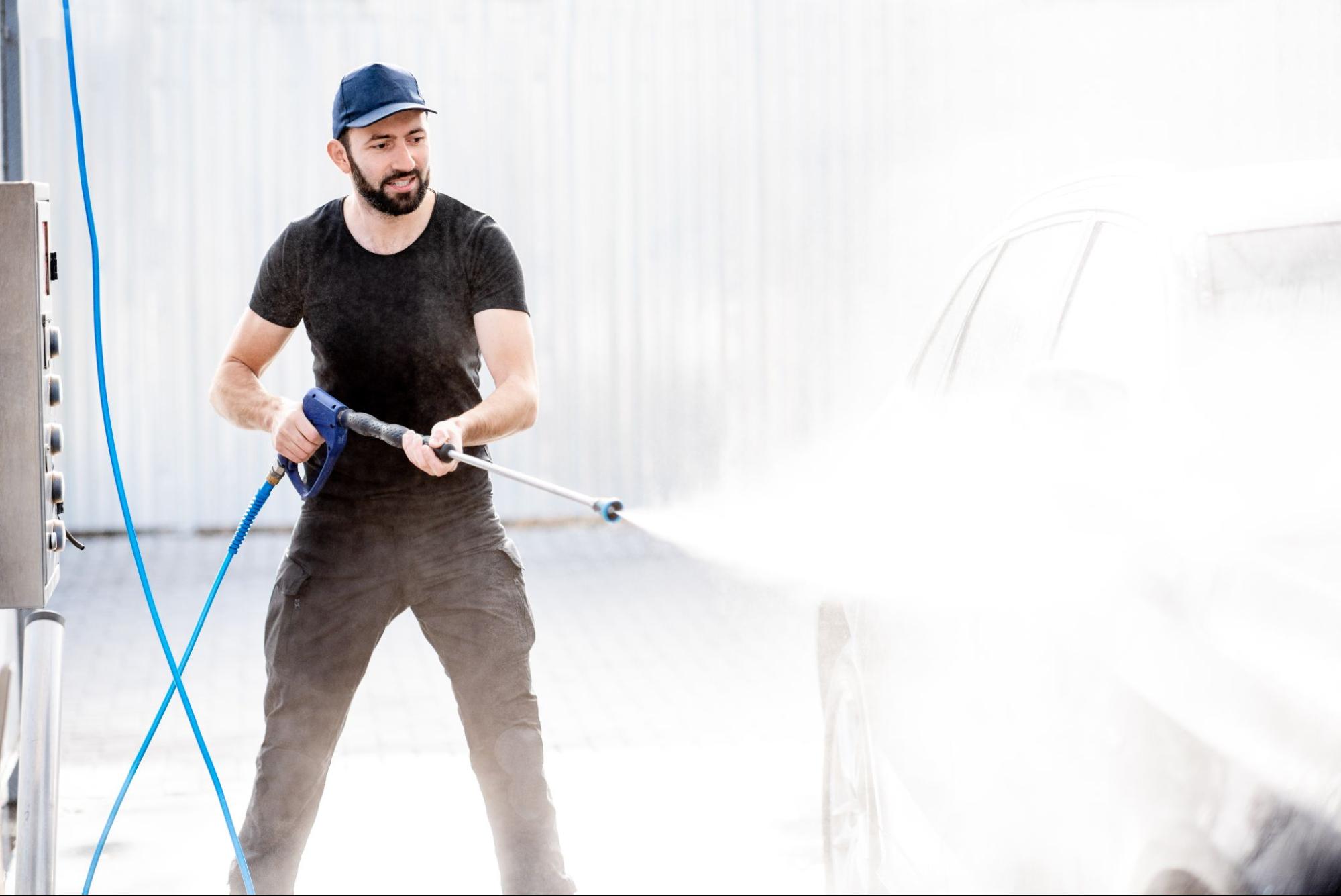 A man washes a car with a pressure washer.