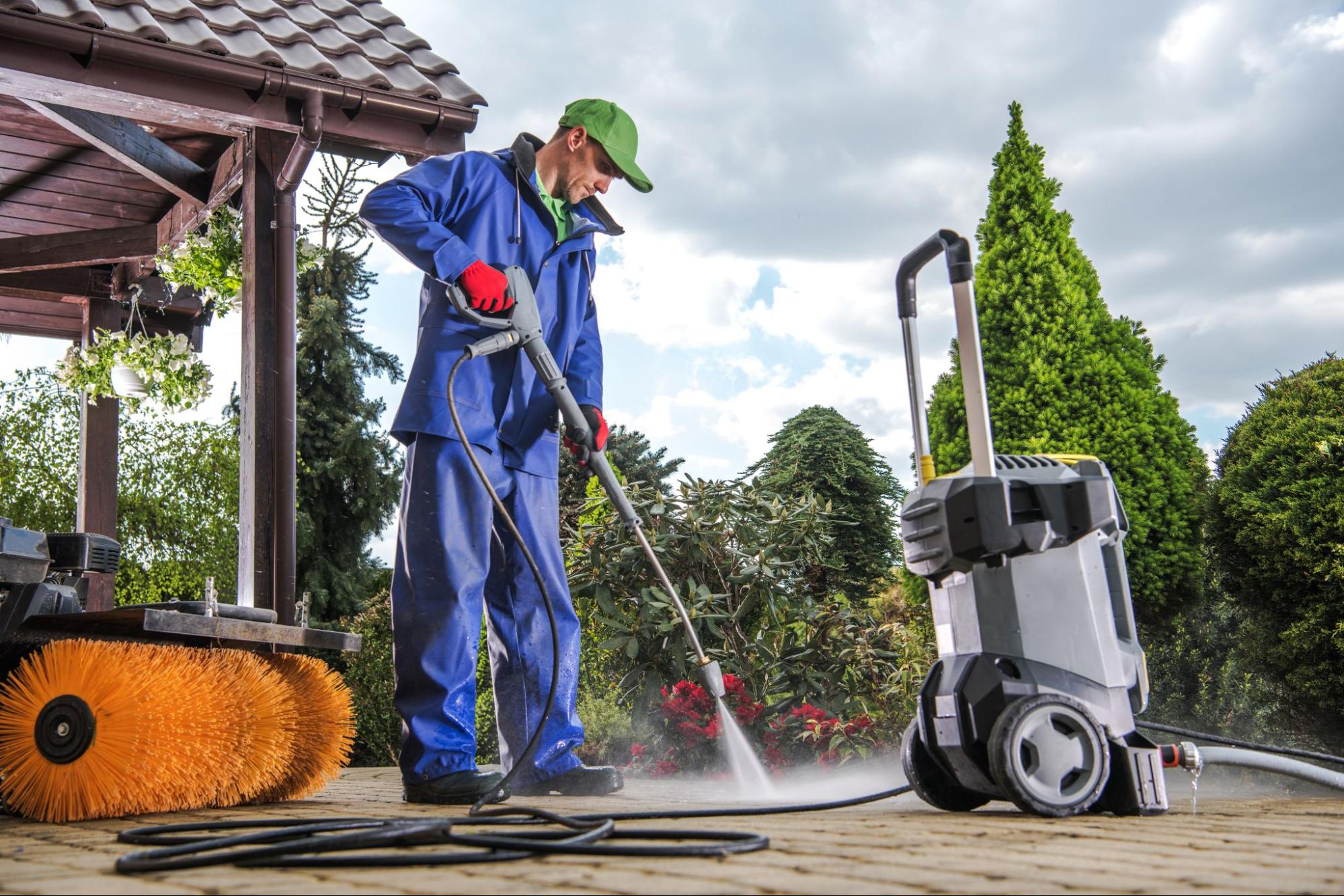 A technician cleaning a brick driveway and pathway using professional pressure washing equipment