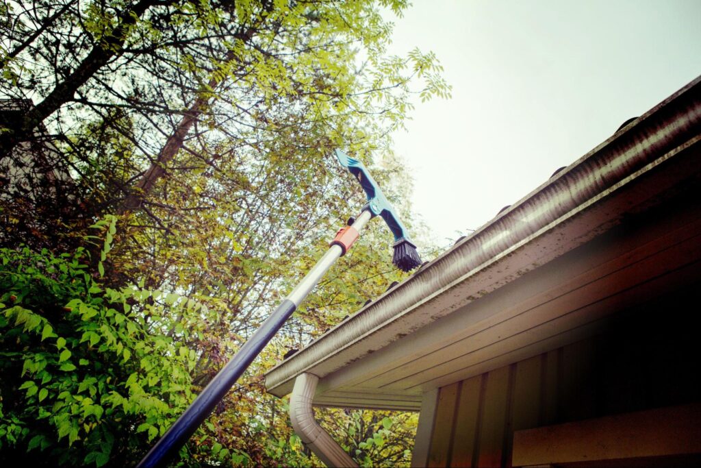 A specialized brush tool with a long arm is used to clean a home’s gutters.