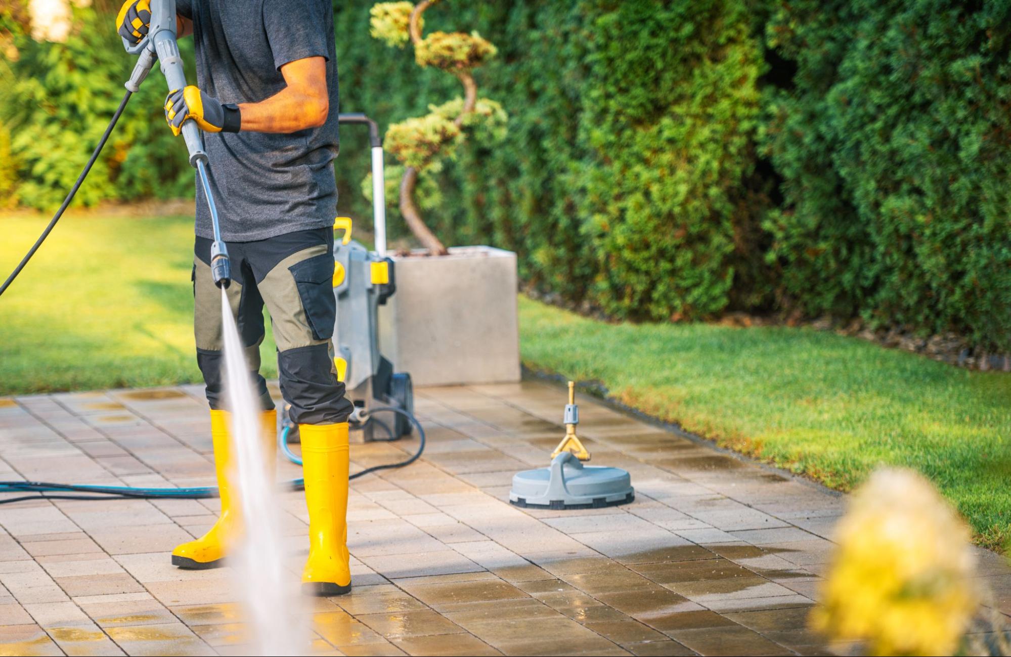 Professional cleaner pressure washing a stone patio in a landscaped backyard