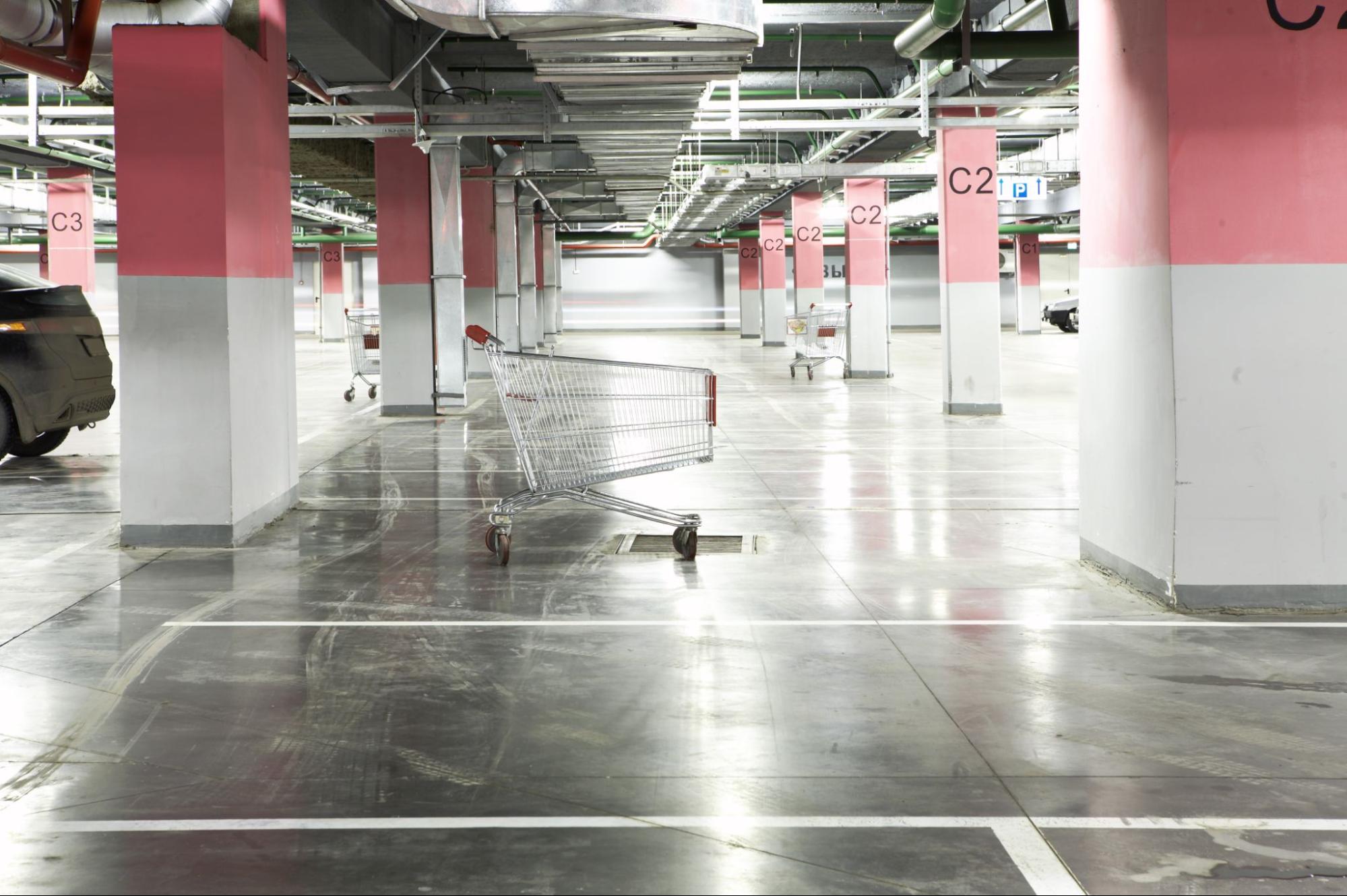 Well-lit underground parking garage with shiny, reflective floors, one grocery cart in the center, and a few others near the support posts.