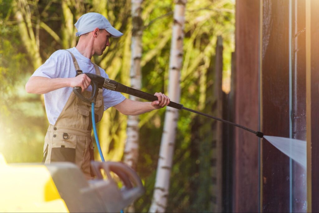 A professional cleaner washes the exterior house walls with a pressure washer
