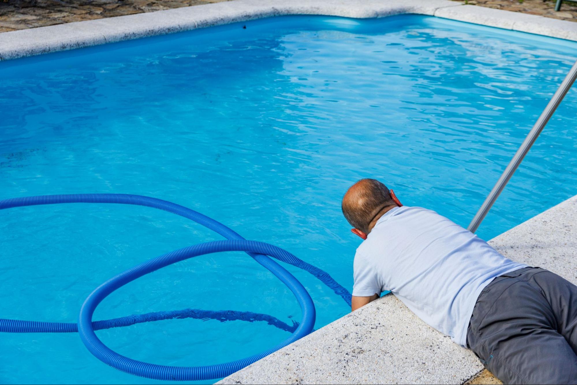 Man holding a hose filling a swimming pool with water, with a cleaning pole nearby