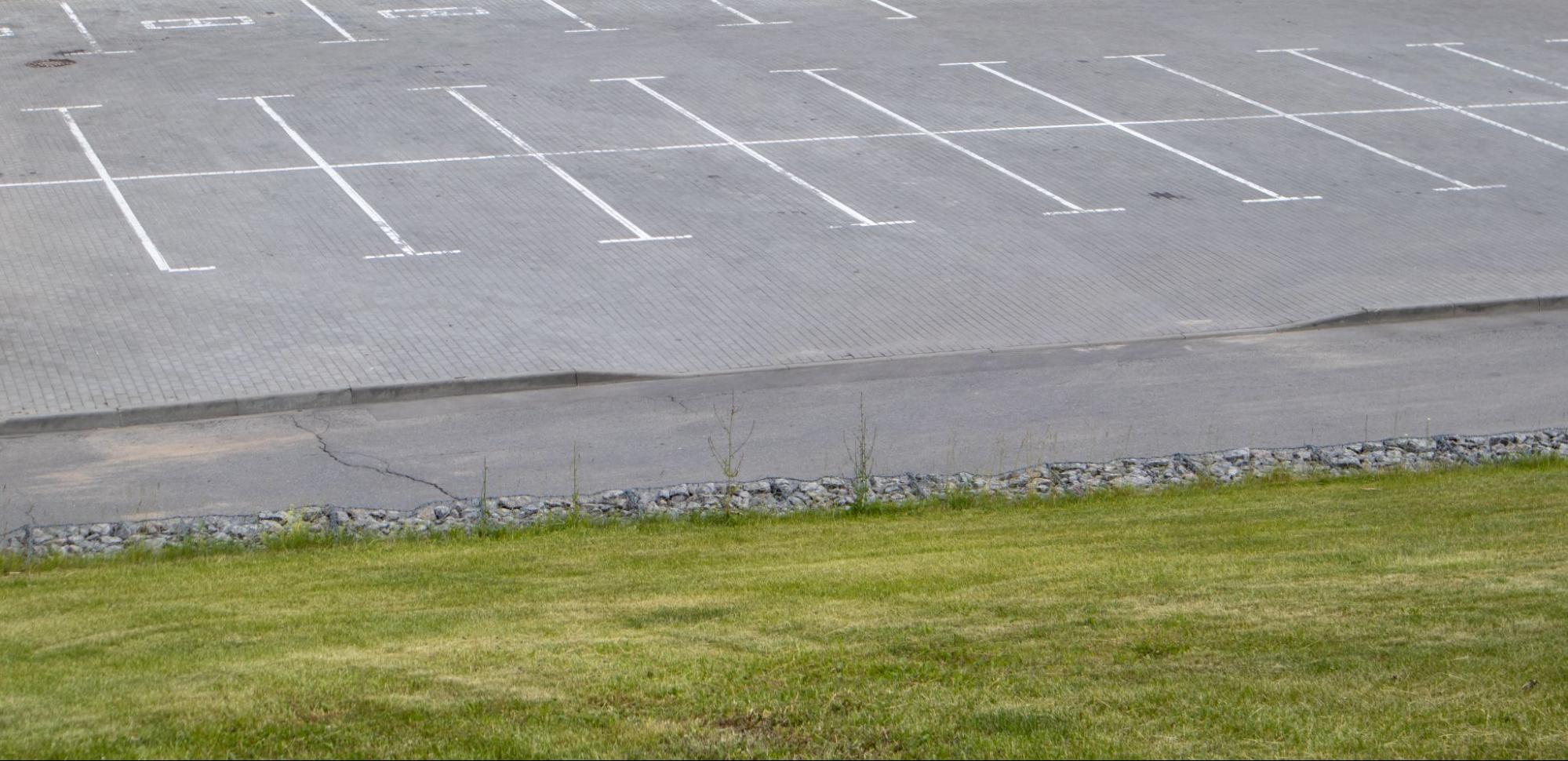 A wide, freshly cleaned parking lot with bright white parking lines and green grass visible in the foreground