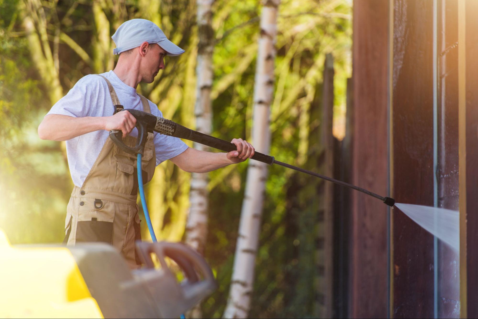 A professional cleaner washes the exterior house walls with a pressure washer